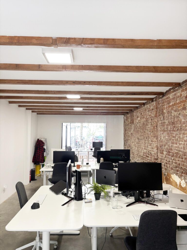 Modern open-plan office on Van Ostadestraat with exposed brick wall, wooden ceiling beams, and multiple workstations.